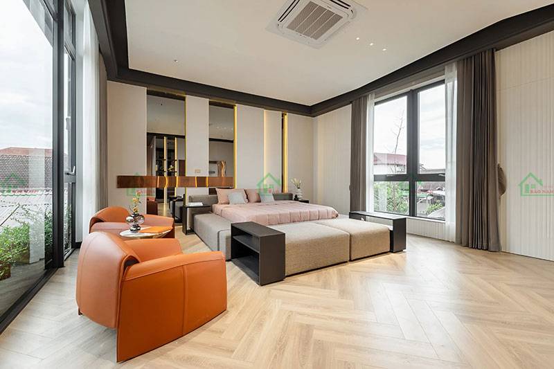 Thiết kế phòng ngủ hiện đại và tinh tế, kết hợp hài hòa giữa giường ngủ thấp, ghế bành, và sàn nhà lát gỗ kiểu xương cá.