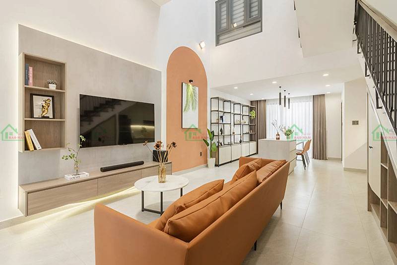 Phòng khách nhà phố hiện đại, thiết kế tối giản với sofa màu cam đất, kệ tivi, và tường trang trí màu sắc ấm áp