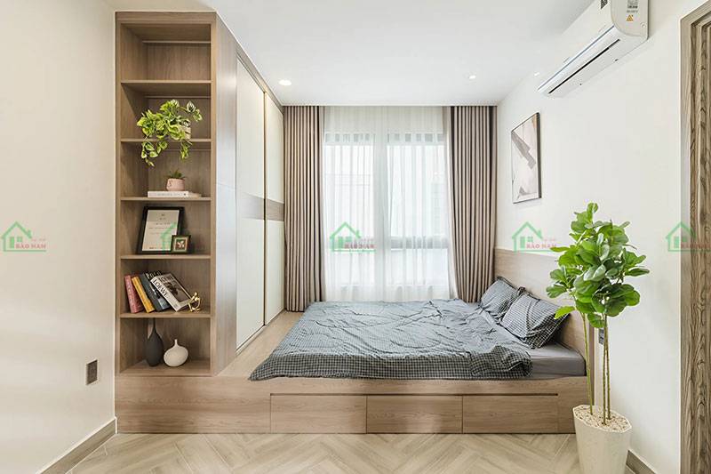Phòng ngủ với giường ngủ thấp tích hợp ngăn kéo, tủ quần áo âm tường cùng tông màu gỗ tự nhiên, và kệ sách liền kề
