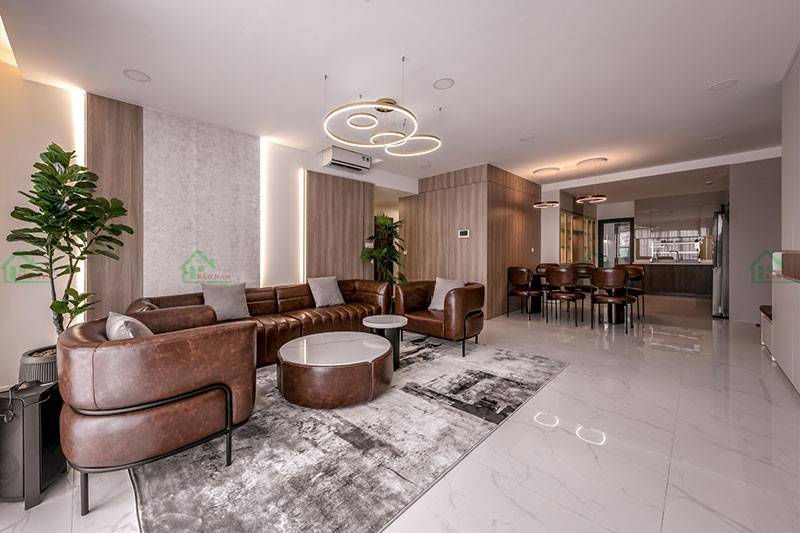 Phòng khách hiện đại, sang trọng với bộ sofa da nâu, sàn đá sáng bóng, và hệ thống đèn ấn tượng